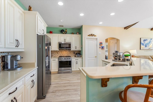 kitchen featuring arched walkways, decorative backsplash, appliances with stainless steel finishes, a breakfast bar, and a sink