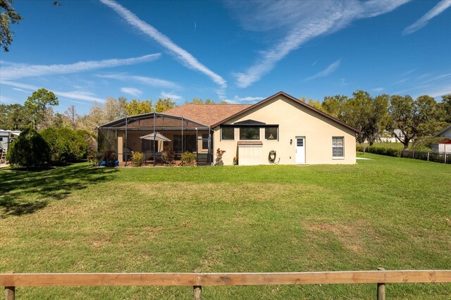 rear view of property featuring glass enclosure, a yard, and stucco siding