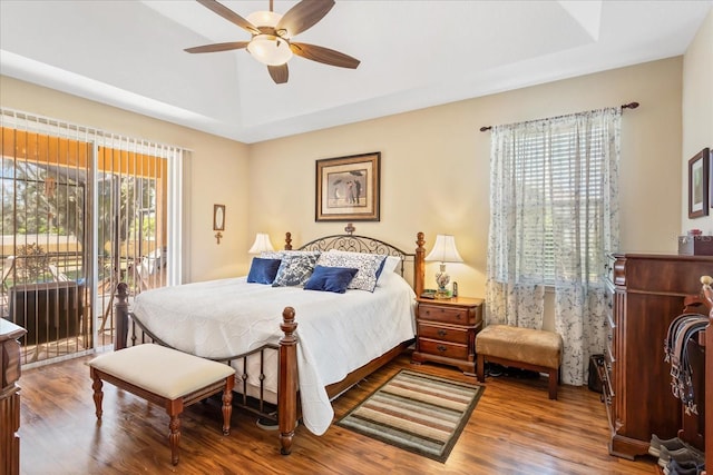 bedroom featuring ceiling fan, access to outside, a tray ceiling, and wood finished floors