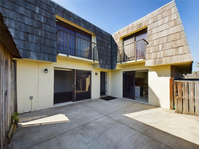 rear view of house with a patio, mansard roof, a balcony, and stucco siding