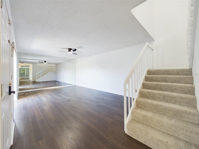 unfurnished living room featuring dark wood-type flooring, stairway, a textured ceiling, and a ceiling fan