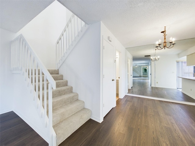 stairs with a chandelier, a textured ceiling, baseboards, and wood finished floors