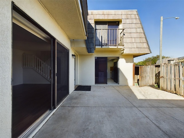 exterior space with a patio, mansard roof, a balcony, fence, and stucco siding