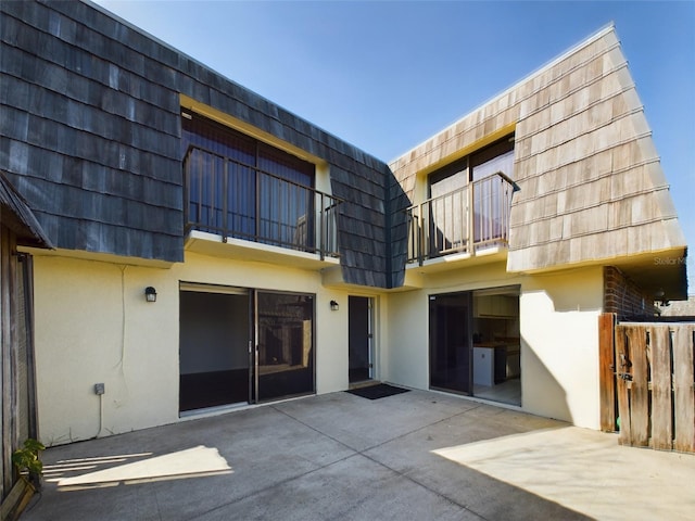 back of house featuring a patio area, stucco siding, a balcony, and mansard roof