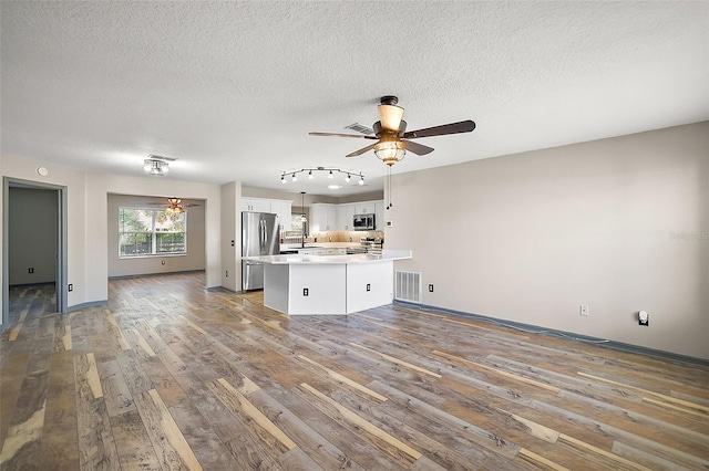 unfurnished living room featuring ceiling fan, dark wood-type flooring, a textured ceiling, and visible vents