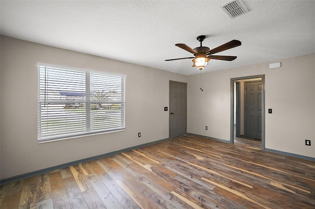 unfurnished room featuring dark wood-style floors, baseboards, visible vents, and a textured ceiling