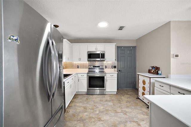 kitchen featuring stainless steel appliances, tasteful backsplash, light countertops, visible vents, and white cabinetry