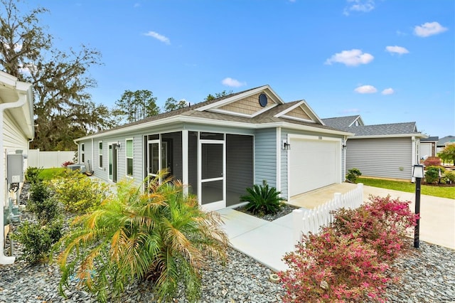 view of front of home with an attached garage, a sunroom, driveway, and fence