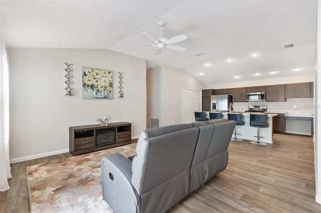 living room featuring light wood-style floors, visible vents, vaulted ceiling, and a ceiling fan