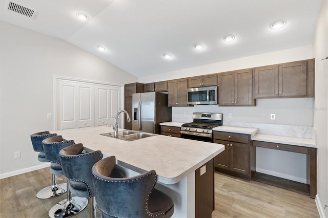 kitchen with a breakfast bar area, stainless steel appliances, lofted ceiling, light countertops, and a kitchen island with sink