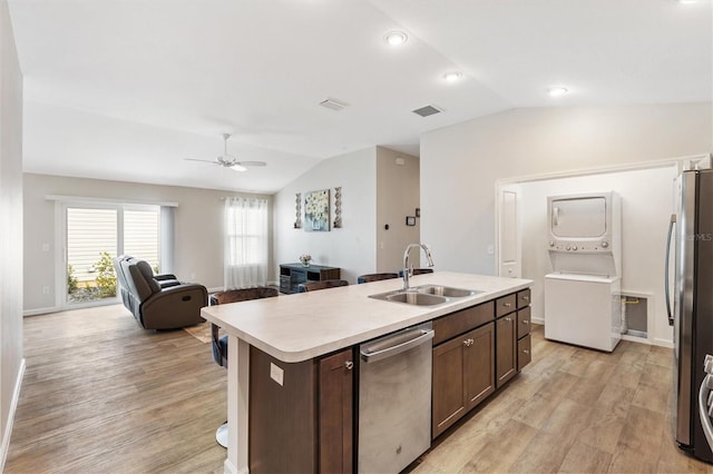 kitchen with open floor plan, light countertops, appliances with stainless steel finishes, an island with sink, and stacked washer and clothes dryer