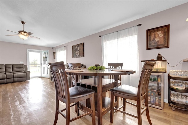 dining space featuring light wood-style flooring, beverage cooler, and a ceiling fan