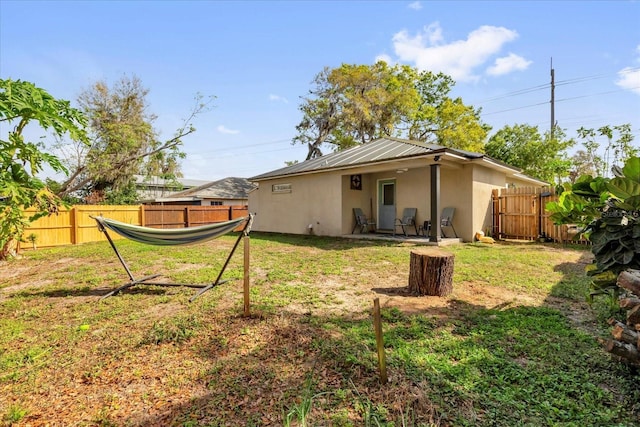 back of property featuring fence, metal roof, a lawn, and stucco siding