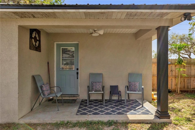 doorway to property with ceiling fan, fence, and stucco siding