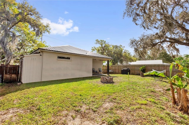 rear view of house featuring an outdoor fire pit, a fenced backyard, metal roof, a yard, and stucco siding