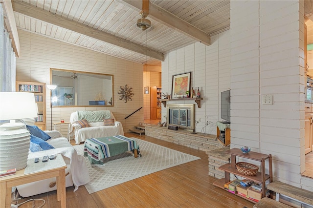 living area featuring a glass covered fireplace, lofted ceiling with beams, and wood finished floors