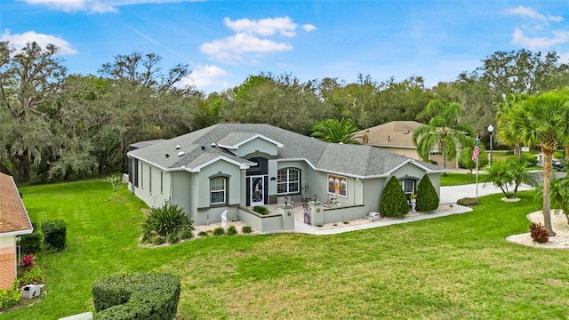 ranch-style home featuring stucco siding, roof with shingles, and a front yard