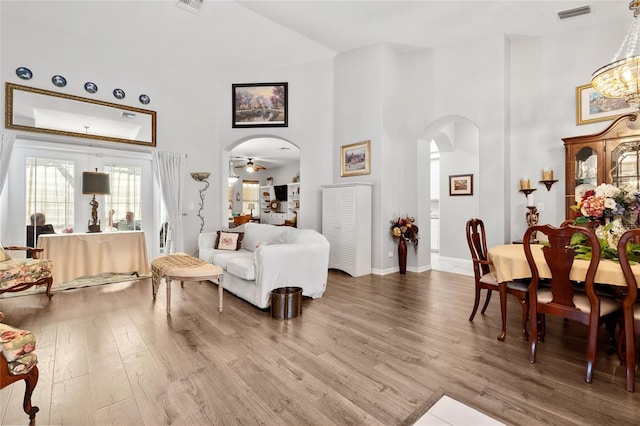 living room with arched walkways, a towering ceiling, wood finished floors, and visible vents