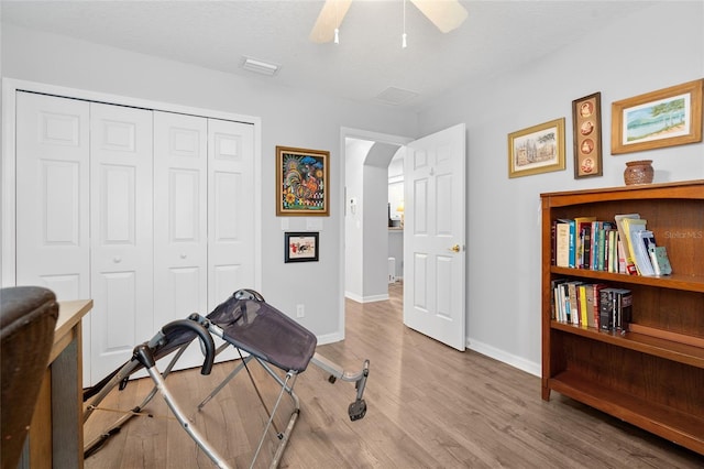 workout area featuring arched walkways, ceiling fan, a textured ceiling, wood finished floors, and baseboards