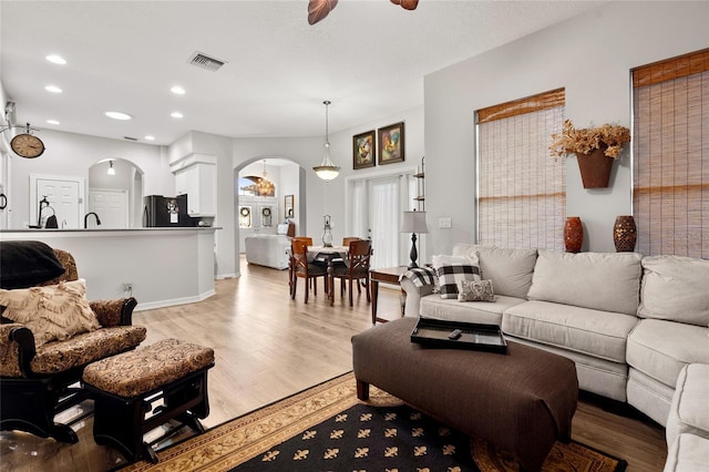 living room with arched walkways, light wood finished floors, recessed lighting, visible vents, and a ceiling fan