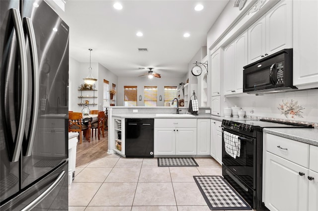 kitchen with light tile patterned floors, a peninsula, a sink, white cabinetry, and black appliances