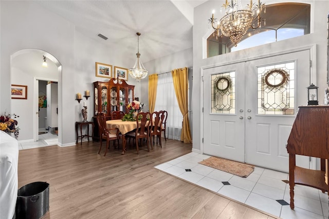 foyer entrance featuring arched walkways, a notable chandelier, wood finished floors, a towering ceiling, and visible vents