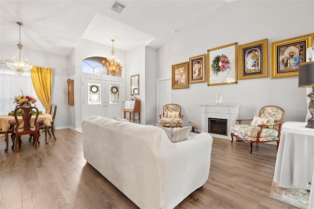 living room with light wood-style floors, visible vents, a fireplace, and a chandelier