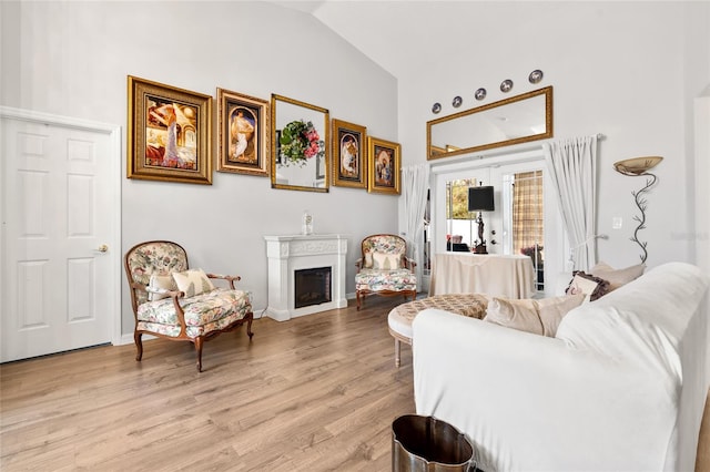 living room featuring light wood-style floors, a fireplace, high vaulted ceiling, and baseboards