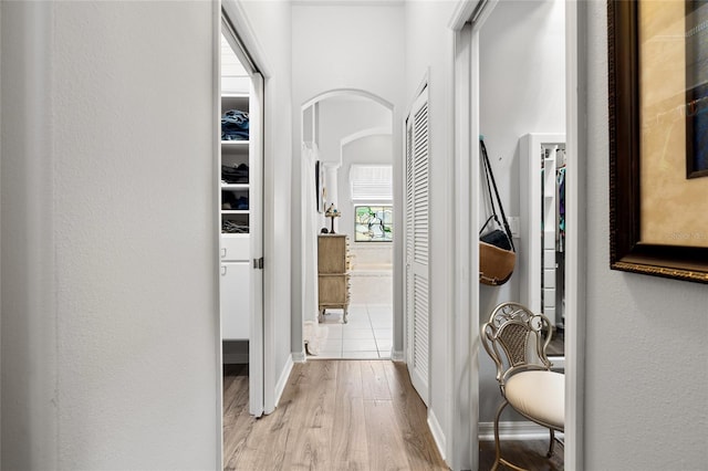 hall featuring arched walkways, light wood-type flooring, and baseboards