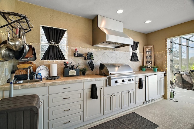 kitchen with tasteful backsplash, wall chimney exhaust hood, light countertops, fridge, and a sink