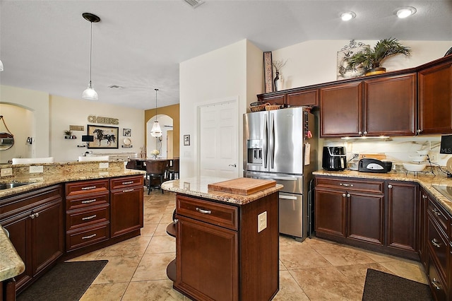 kitchen with arched walkways, decorative light fixtures, stainless steel refrigerator with ice dispenser, and light stone countertops