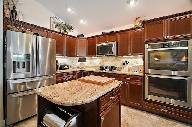 kitchen with a kitchen island, light stone counters, vaulted ceiling, stainless steel appliances, and light tile patterned flooring