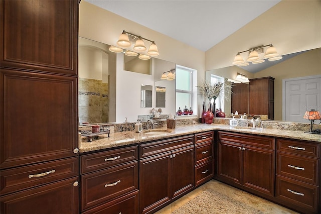 full bath with double vanity, vaulted ceiling, and a sink