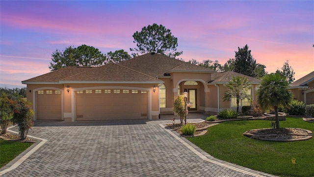 view of front of house featuring a garage, a front yard, decorative driveway, and stucco siding