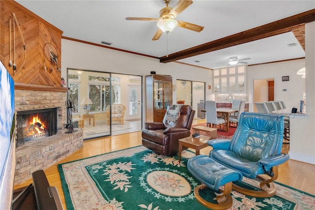 living room featuring ceiling fan, a fireplace, wood finished floors, visible vents, and crown molding