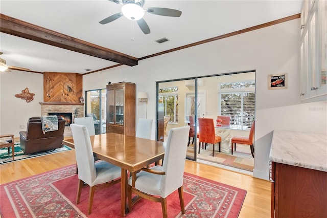 dining space with light wood-type flooring, a healthy amount of sunlight, and a stone fireplace