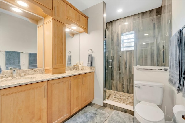 full bath featuring double vanity, toilet, a shower stall, a sink, and recessed lighting