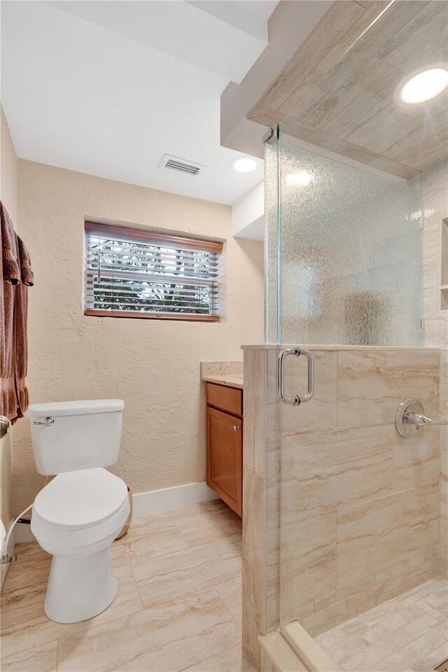 bathroom featuring visible vents, a textured wall, toilet, a stall shower, and baseboards