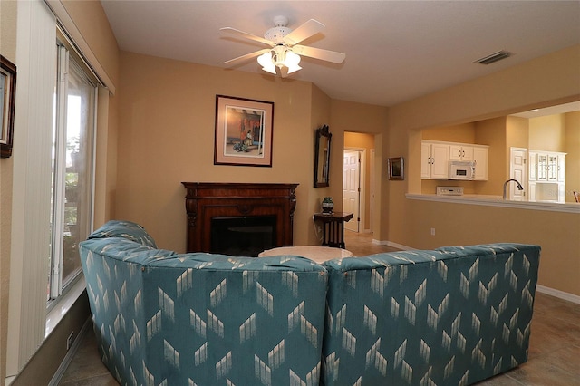 tiled living area featuring baseboards, visible vents, a ceiling fan, a fireplace, and a sink