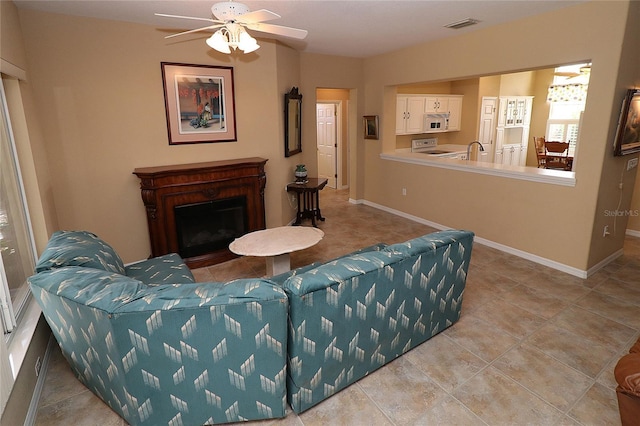 tiled living room with a fireplace, visible vents, a ceiling fan, a sink, and baseboards