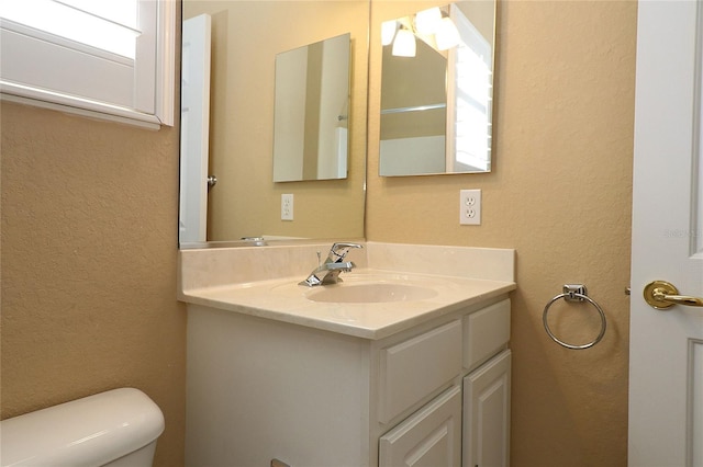 half bath featuring a textured wall, vanity, and toilet