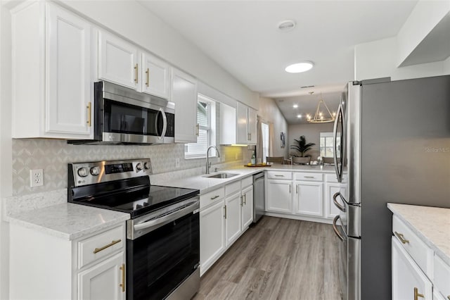 kitchen featuring light wood finished floors, white cabinets, appliances with stainless steel finishes, a sink, and backsplash