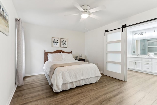 bedroom with a barn door, a ceiling fan, baseboards, light wood-type flooring, and ensuite bath