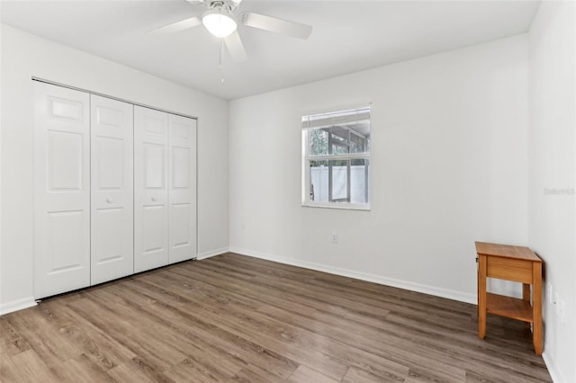 unfurnished bedroom with a closet, wood finished floors, a ceiling fan, and baseboards