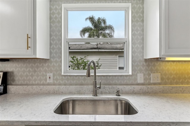 kitchen with light stone counters, white cabinets, a sink, and backsplash