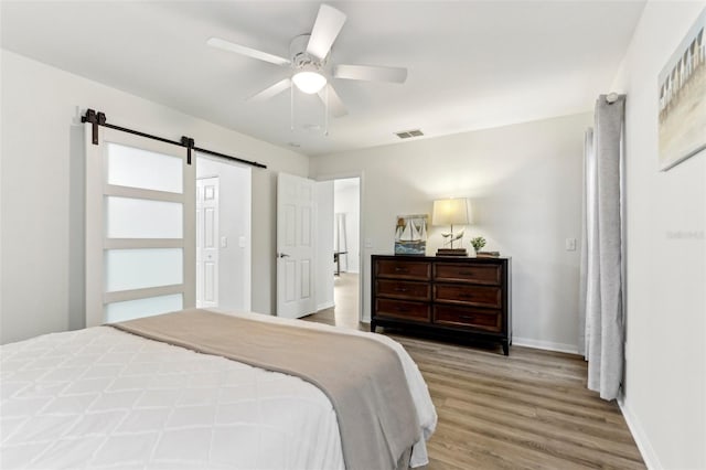 bedroom featuring visible vents, a barn door, ceiling fan, wood finished floors, and baseboards