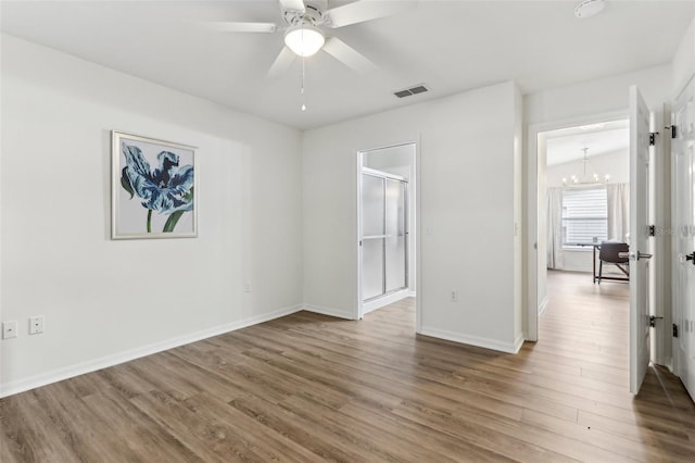 unfurnished room with baseboards, visible vents, wood finished floors, and ceiling fan with notable chandelier