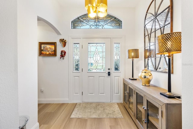 entryway featuring light wood-style floors, baseboards, arched walkways, and a notable chandelier