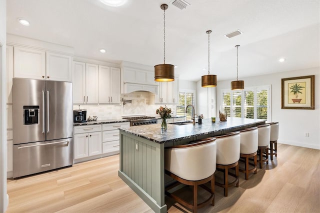 kitchen with a sink, visible vents, high end fridge, light wood finished floors, and tasteful backsplash