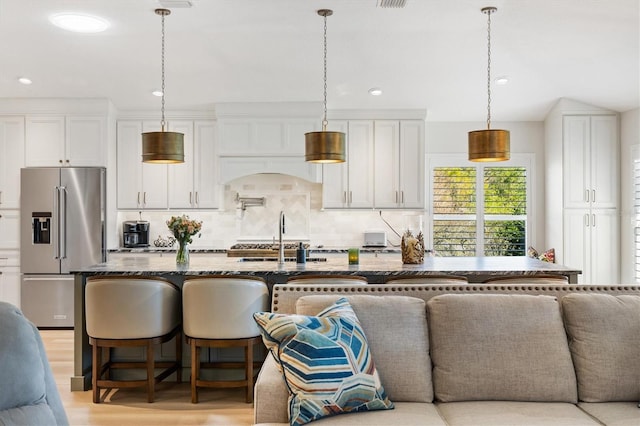 kitchen with high quality fridge, white cabinets, dark stone counters, light wood finished floors, and tasteful backsplash